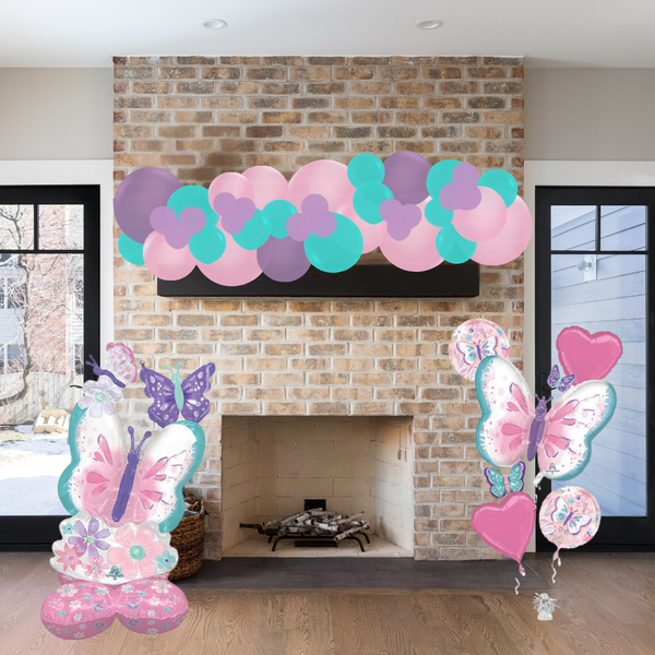 Decorative balloon arch with pink, purple, and teal balloons above a fireplace.
