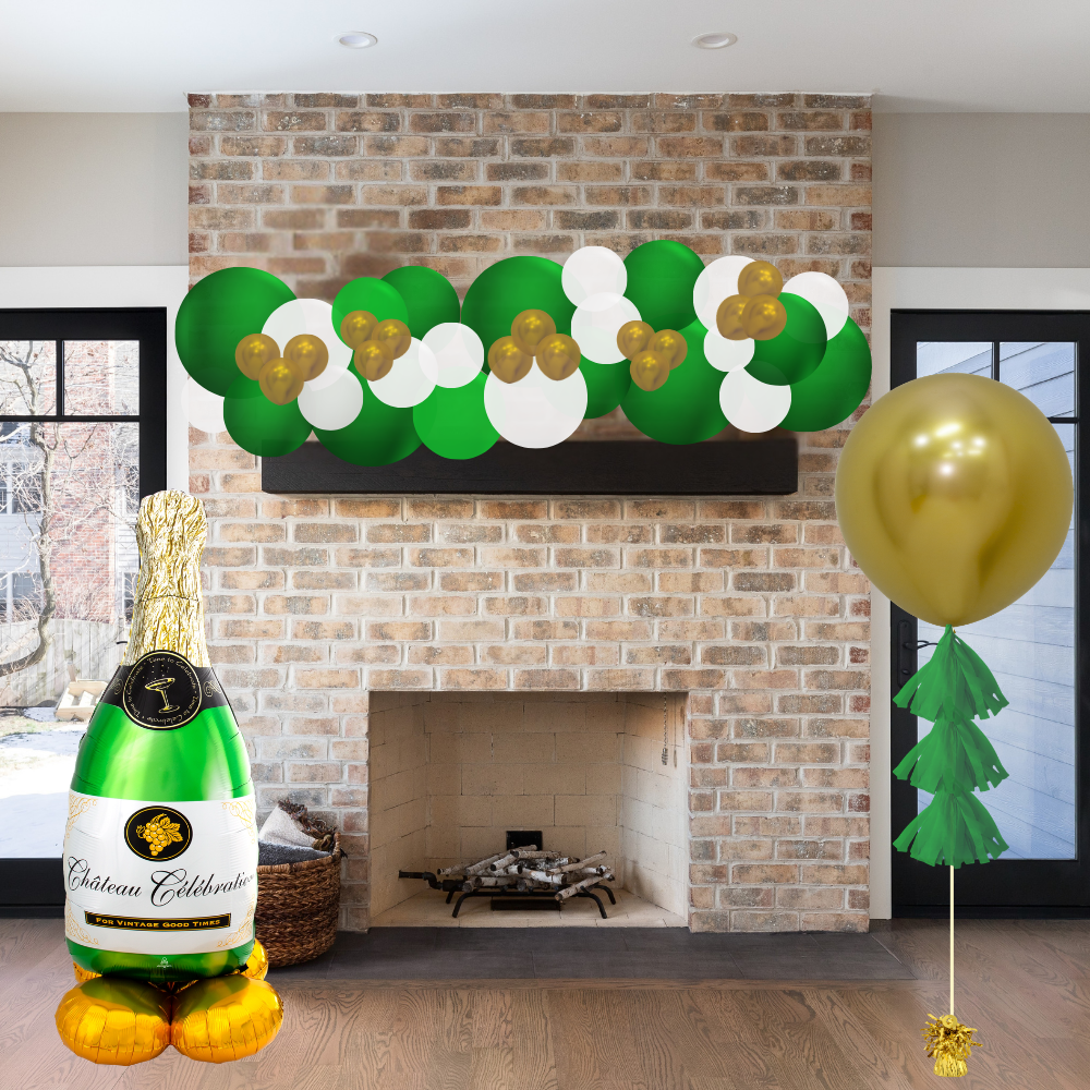 Decorative setup with champagne bottle balloon, green and gold balloons, and festive decorations in front of a brick fireplace.