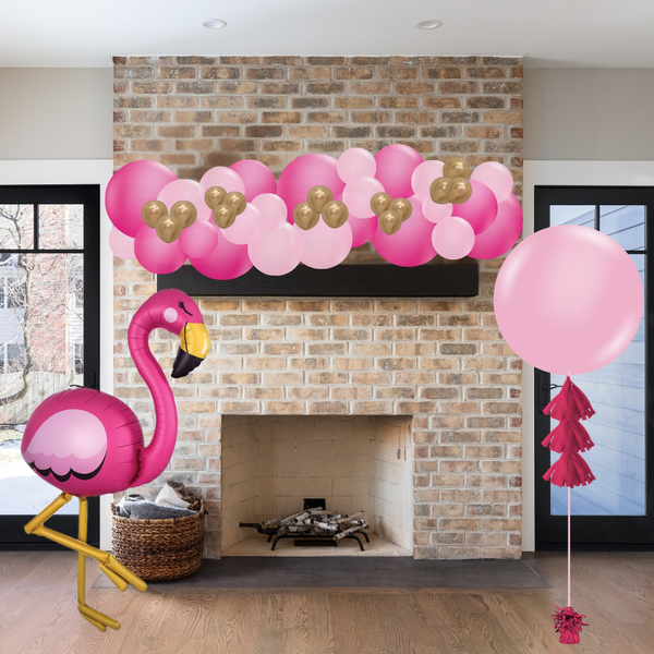 Decorative setup with pink balloons, flamingo, and tassel in front of a brick fireplace.