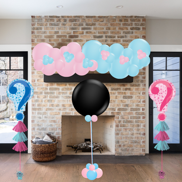 Balloon arch with pink, blue, and black balloons in front of a brick fireplace.