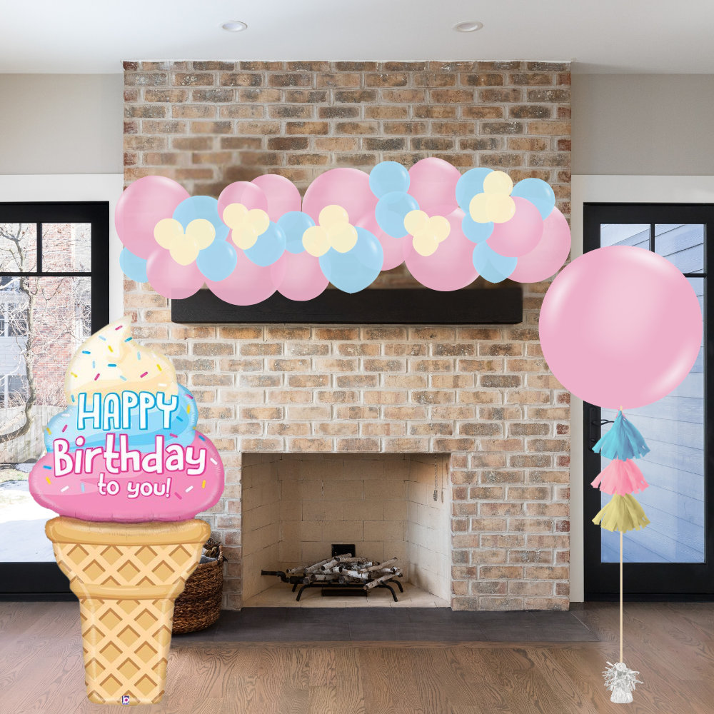 Decorative birthday setup with ice cream cone, balloons, and garland in front of a fireplace.