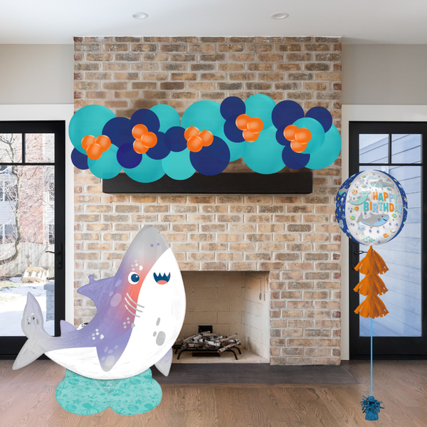 Decorative shark balloon and birthday balloons in front of a brick fireplace.