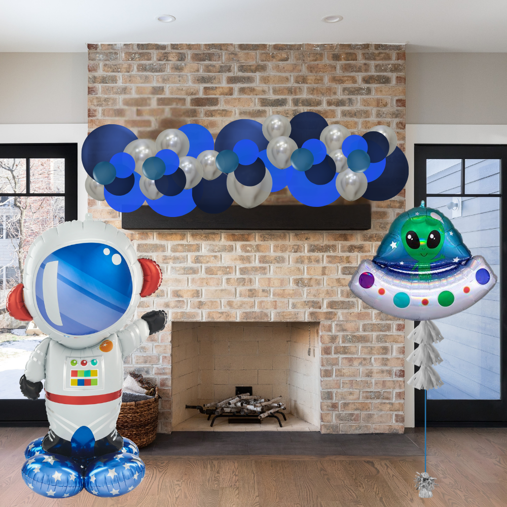 Decorative balloons shaped like an astronaut and a UFO in front of a brick fireplace.